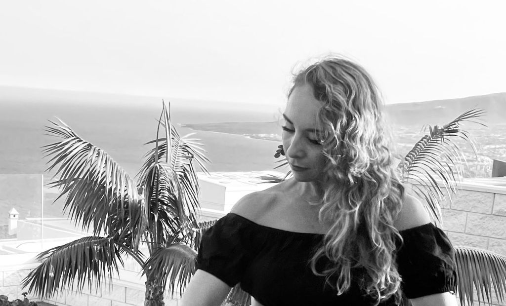 Una foto de Carmela Visone en blanco y negro con dos palmeras detrás y con un vista al mar.